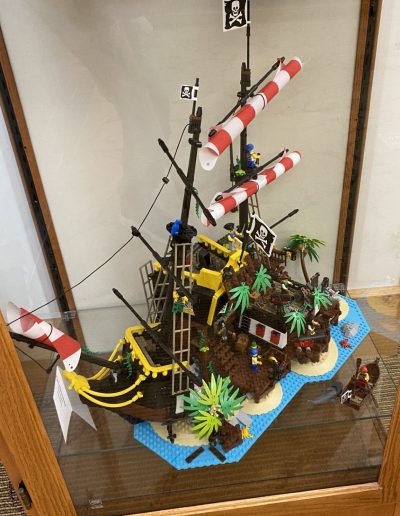 A Lego pirate ship showcased in a glass case, complete with tiny sails and cannons.