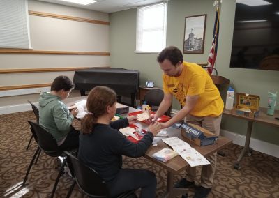 At a table, a man helps two children assemble a STEAM kit.