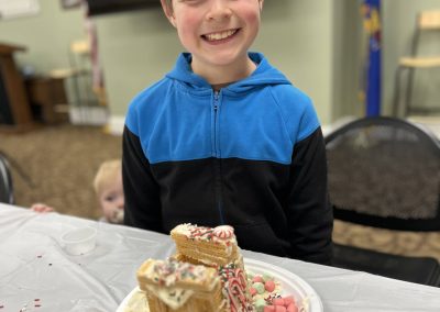 A young boy smiles proudly while holding a plate of gingerbread, showcasing his festive gingerbread house creation.