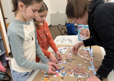 A trio of girls focused on completing a puzzle, surrounded by colorful pieces, and sharing a fun, collaborative moment.