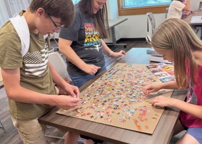 Three people work on a jigsaw puzzle at a table in a bright room.