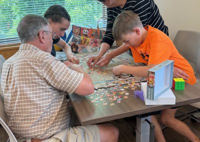 Four people working on a jigsaw puzzle at a table next to a window.
