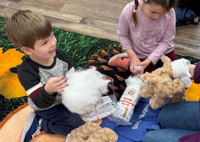 Two children are stuffing teddy bears with craft materials around them.