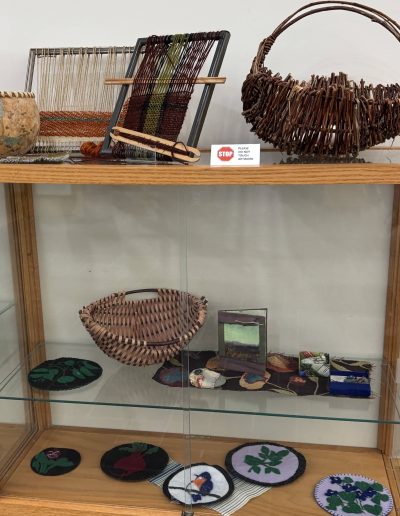 Museum display case containing woven baskets, looms, textile artworks, and a “Please Do Not Touch Artwork” sign.